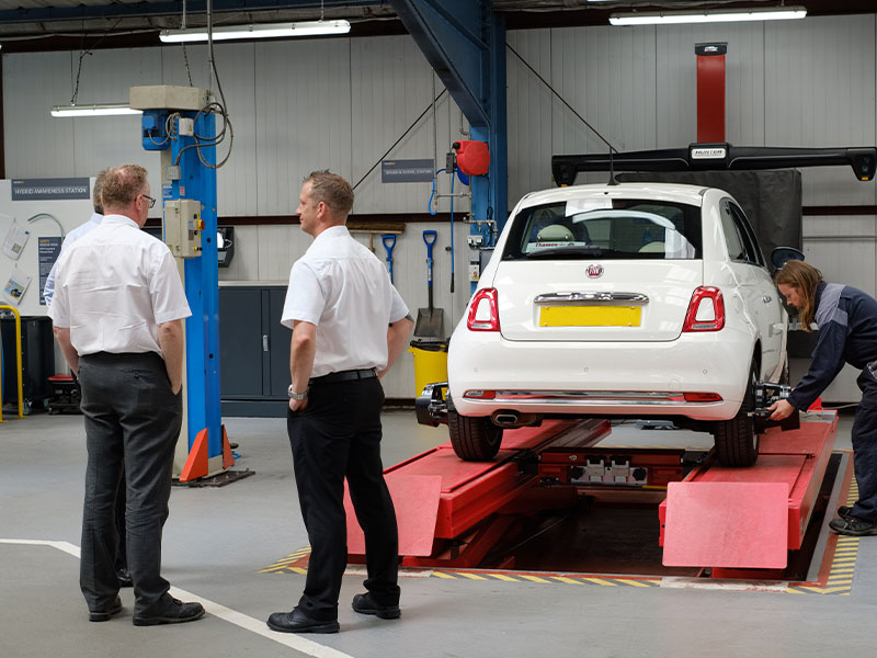 Two men standing by a white car in a car garage